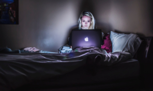 Frau sitzt im Dunkeln mit Laptop auf dem Bett