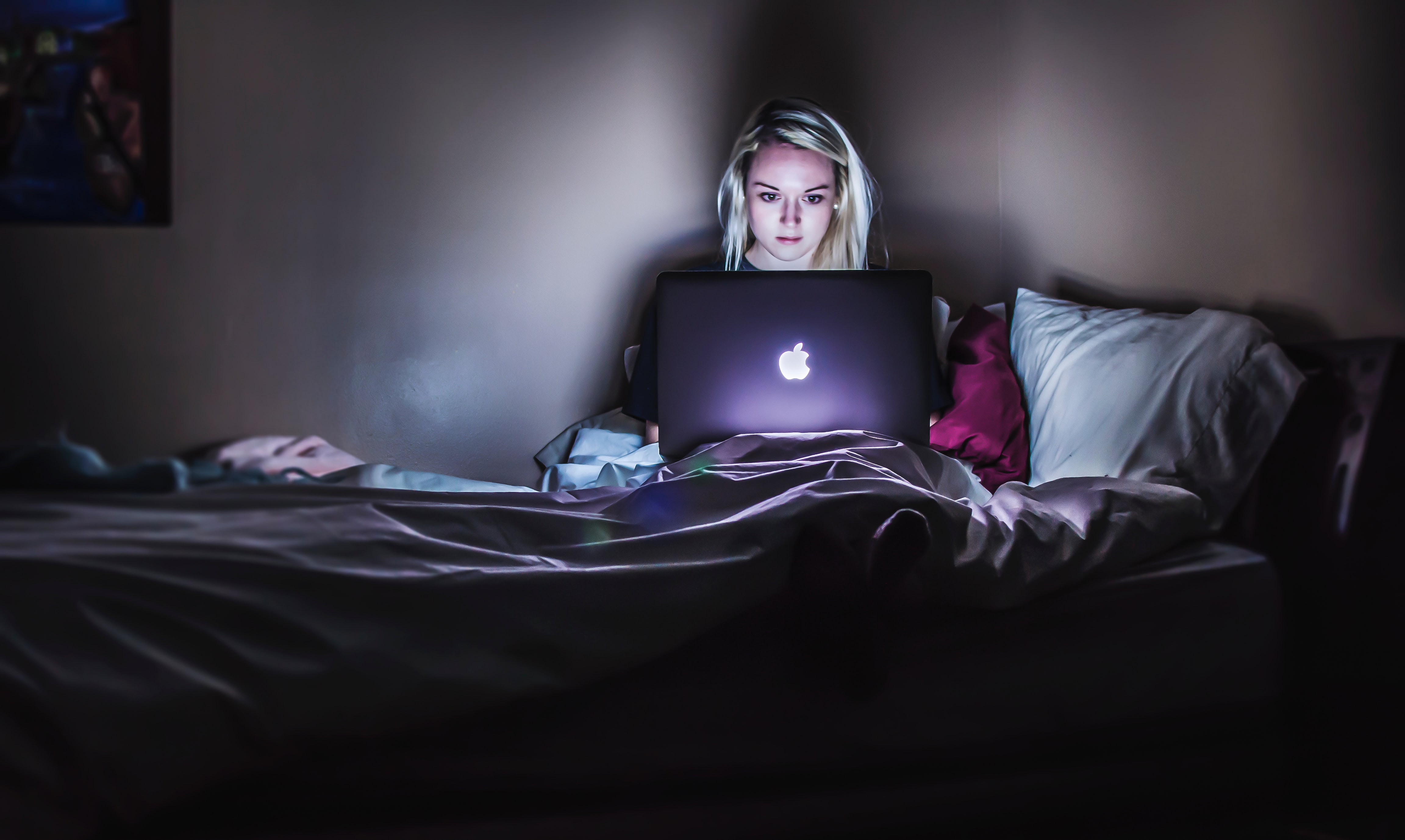 Frau sitzt im Dunkeln mit Laptop auf dem Bett